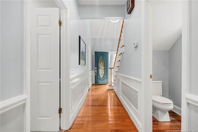 hallway featuring a decorative wall, stairway, light wood-style floors, and wainscoting
