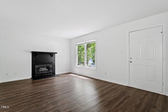 unfurnished living room with dark wood-type flooring, a glass covered fireplace, and baseboards