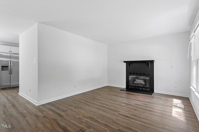 unfurnished living room with dark wood finished floors, a glass covered fireplace, and baseboards