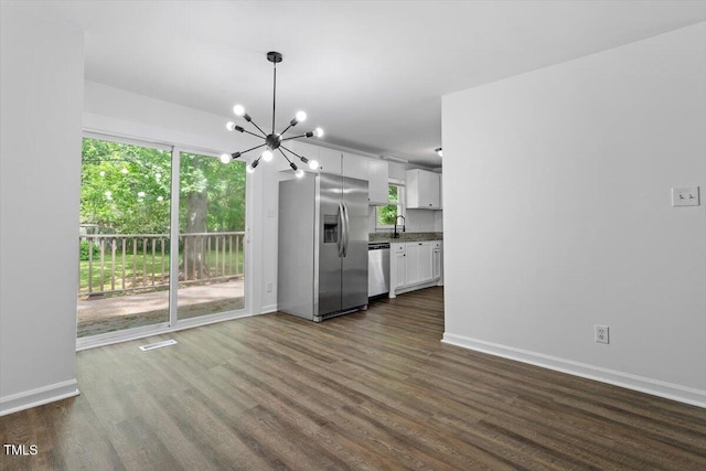 unfurnished dining area featuring a chandelier, dark wood-type flooring, and plenty of natural light
