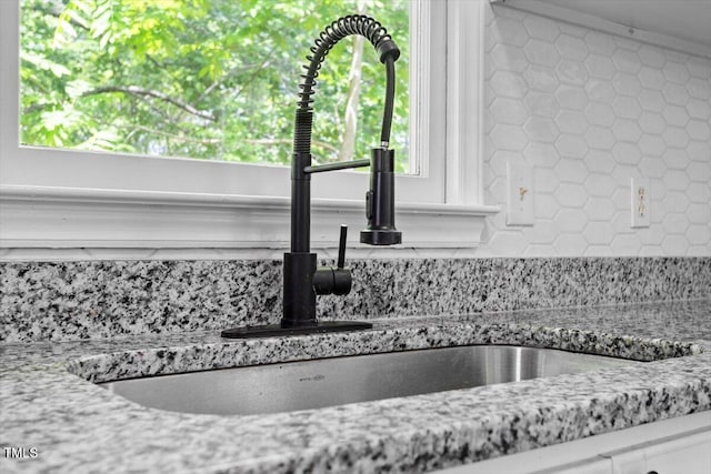 kitchen view of a sink, backsplash, and light stone counters