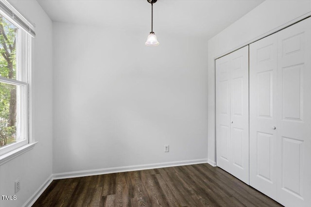 unfurnished bedroom with dark wood-type flooring, a closet, and baseboards