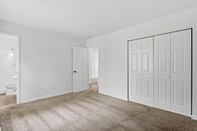 unfurnished bedroom with carpet flooring, a closet, baseboards, and ensuite bathroom