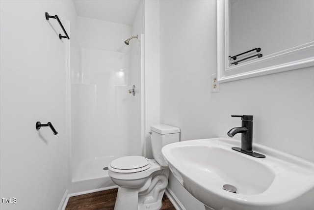 bathroom featuring a sink, a shower, toilet, wood finished floors, and baseboards