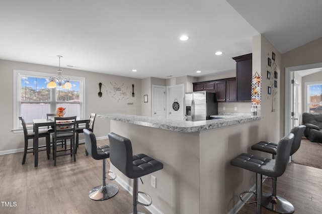 kitchen featuring stainless steel fridge, a kitchen bar, baseboards, a chandelier, and light wood-type flooring
