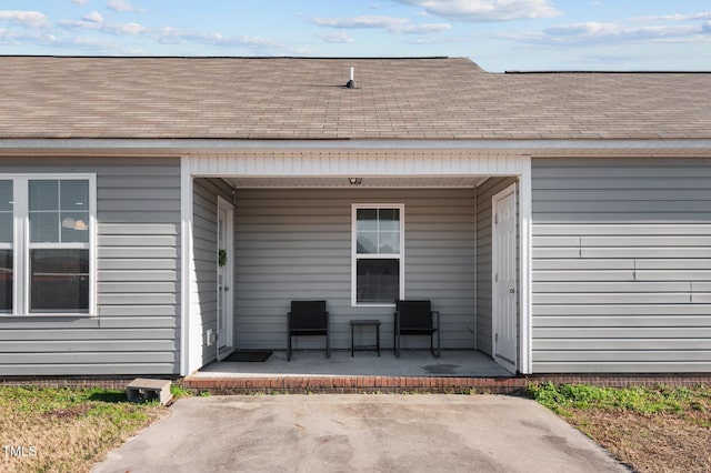 view of exterior entry with roof with shingles and covered porch