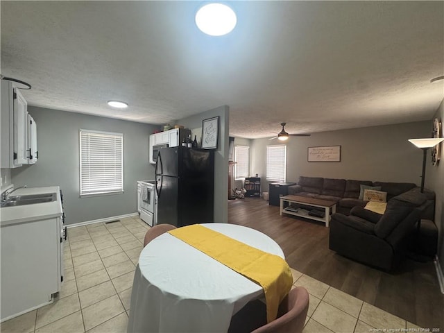 kitchen with freestanding refrigerator, a sink, light tile patterned floors, white cabinetry, and light countertops