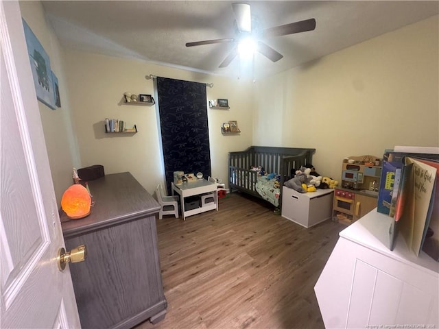 bedroom with wood finished floors, a nursery area, and a ceiling fan
