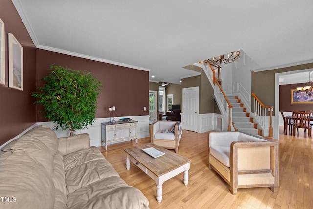 living area featuring a chandelier, crown molding, light wood-style flooring, a wainscoted wall, and stairs