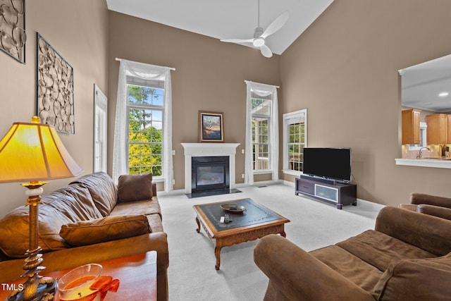 living area with light carpet, a ceiling fan, a fireplace with flush hearth, high vaulted ceiling, and baseboards