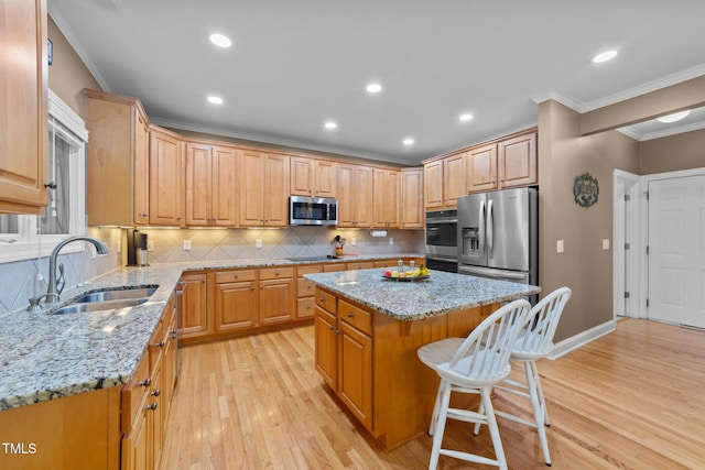 kitchen with a sink, stainless steel appliances, a center island, light wood finished floors, and ornamental molding