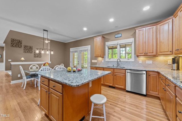 kitchen featuring dishwasher, a sink, light wood-type flooring, a center island, and ornamental molding