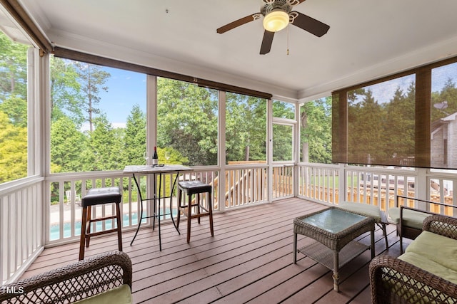 sunroom featuring ceiling fan and view of wooded area