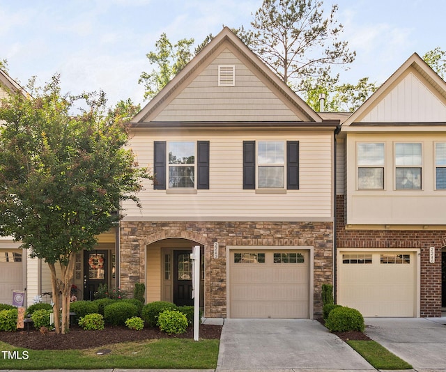 townhome / multi-family property with driveway, a garage, and stone siding
