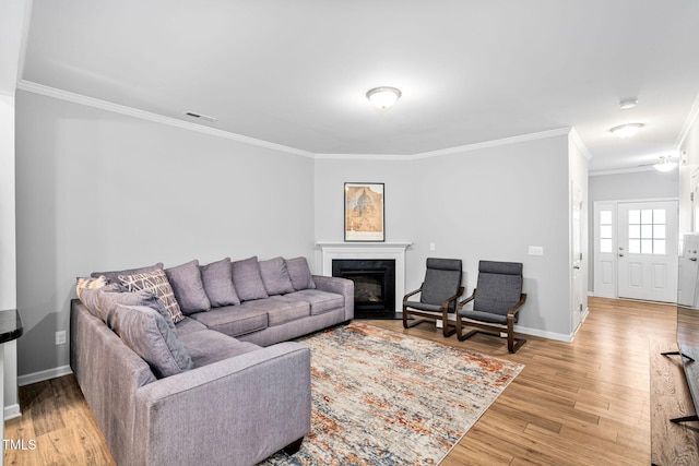 living area featuring ornamental molding, light wood-style flooring, baseboards, and a glass covered fireplace