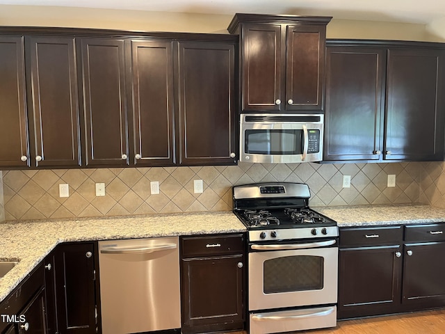 kitchen with stainless steel appliances, light stone countertops, backsplash, and dark brown cabinets