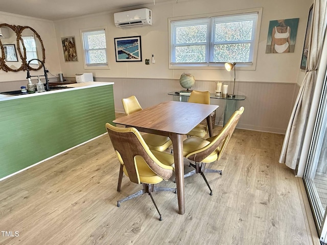 dining space featuring a wall mounted AC, wainscoting, plenty of natural light, light wood-style floors, and crown molding