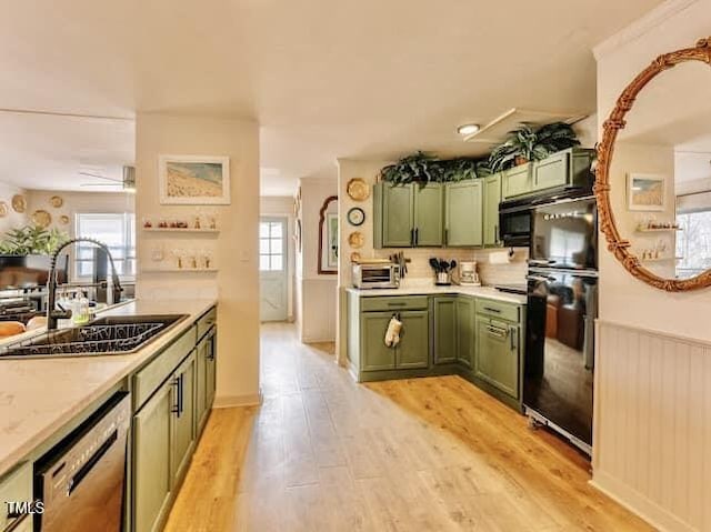 kitchen with green cabinets, a sink, black appliances, light countertops, and light wood-style flooring