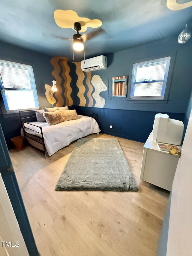 bedroom with a wall mounted air conditioner, multiple windows, wood finished floors, and ceiling fan