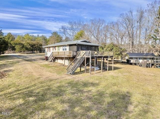 back of house featuring stairway, a sunroom, a deck, and a lawn