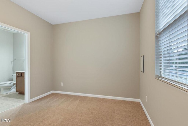 unfurnished bedroom with light colored carpet, baseboards, and connected bathroom