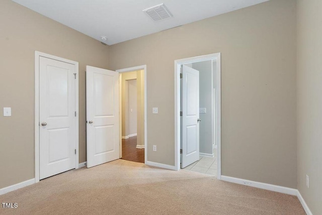 unfurnished bedroom with light colored carpet, baseboards, and ensuite bath