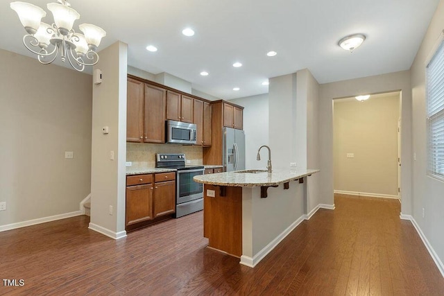 kitchen featuring stainless steel appliances, dark wood-type flooring, brown cabinets, a kitchen bar, and recessed lighting