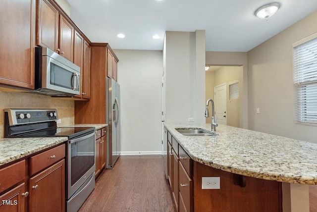 kitchen with appliances with stainless steel finishes, a sink, dark wood-style floors, light stone counters, and baseboards