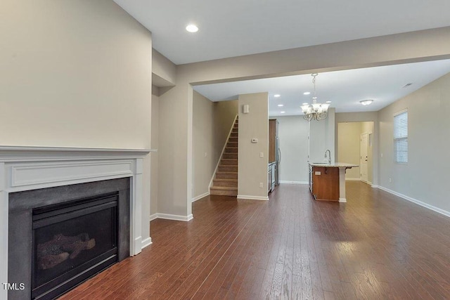 unfurnished living room with stairway, a chandelier, baseboards, dark wood-style flooring, and recessed lighting