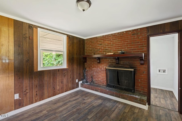 unfurnished living room with a brick fireplace, baseboards, wood finished floors, and wood walls