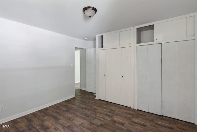 unfurnished bedroom featuring multiple closets, dark wood-style floors, and baseboards