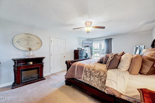 carpeted bedroom featuring a textured ceiling, ceiling fan, a glass covered fireplace, and baseboards