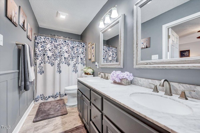 full bath with a textured ceiling, double vanity, and toilet
