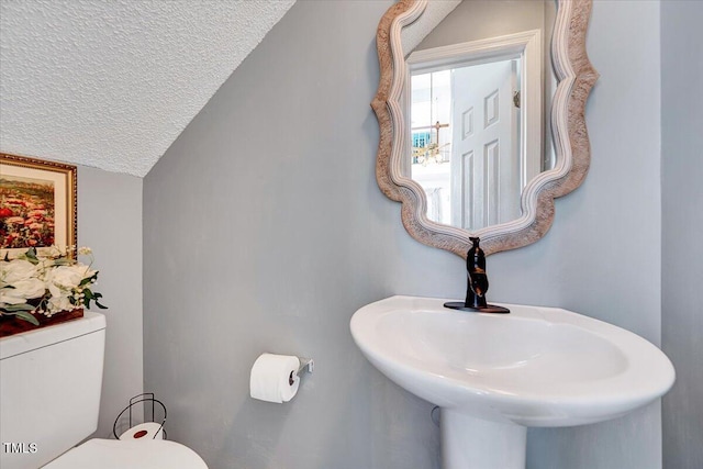 half bath with a textured ceiling, toilet, lofted ceiling, and a sink