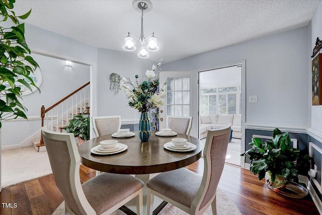 dining space with wood-type flooring, stairs, a chandelier, and a textured ceiling