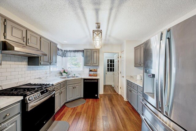 kitchen with appliances with stainless steel finishes, gray cabinetry, a sink, under cabinet range hood, and a textured ceiling