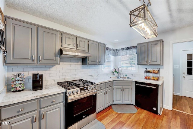 kitchen featuring gray cabinets, dishwasher, stainless steel gas range oven, under cabinet range hood, and a sink