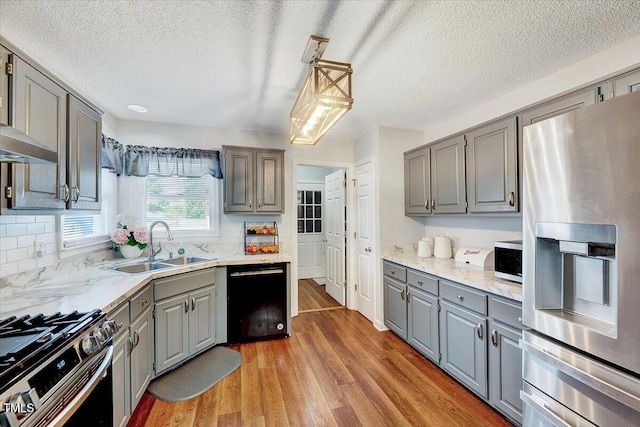kitchen with appliances with stainless steel finishes, gray cabinets, a sink, a textured ceiling, and light wood-style flooring