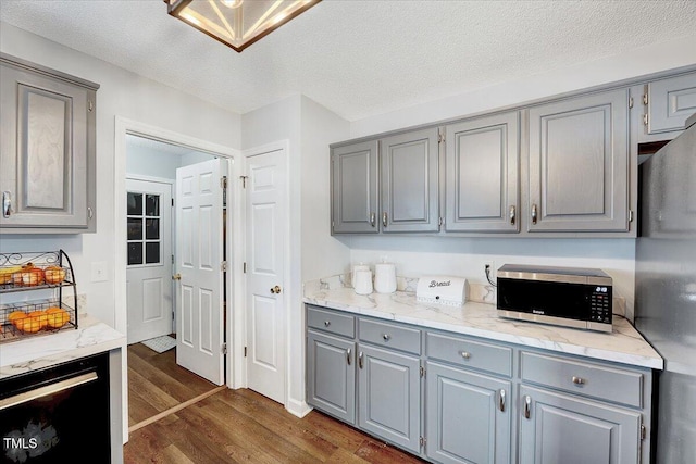 kitchen with gray cabinetry, stainless steel appliances, dark wood-type flooring, a textured ceiling, and light stone counters