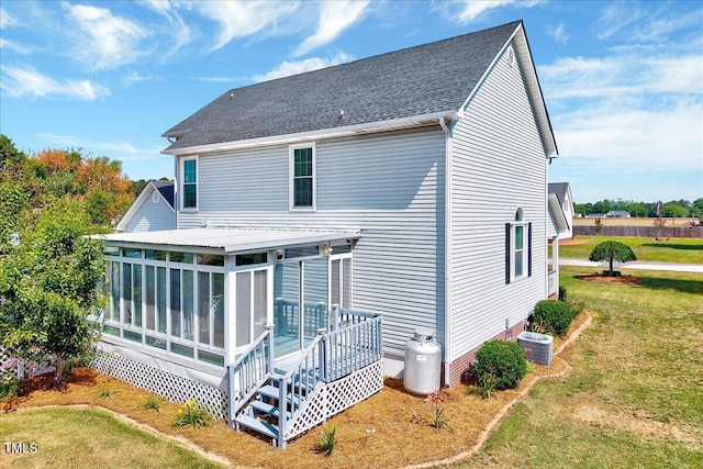 back of property featuring a lawn, a sunroom, a deck, a shingled roof, and central AC unit