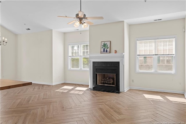 unfurnished living room with ceiling fan, baseboards, a fireplace with flush hearth, and a chandelier
