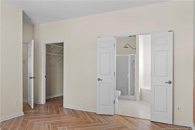 unfurnished bedroom with baseboards, a closet, a walk in closet, and connected bathroom