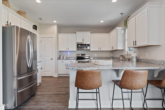 kitchen with appliances with stainless steel finishes, a peninsula, a sink, white cabinets, and recessed lighting