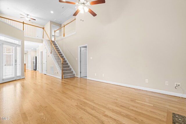 112 River Dell Townes Ave, Clayton, NC 27527 - unfurnished living room featuring a ceiling fan, stairs, a towering ceiling, light wood-style floors, and baseboards