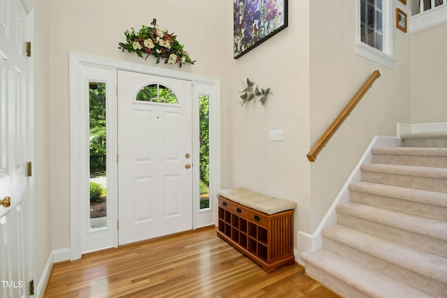foyer entrance featuring light wood-style flooring, stairway, a towering ceiling, and baseboards