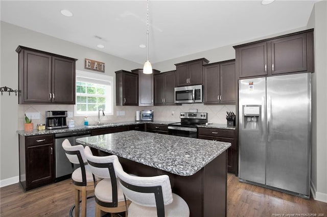 kitchen with appliances with stainless steel finishes, dark brown cabinets, stone countertops, a kitchen island, and dark wood-type flooring