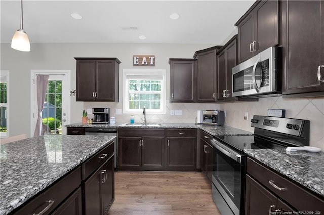 kitchen with stainless steel appliances, a sink, light wood finished floors, dark stone countertops, and recessed lighting