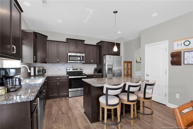 kitchen with appliances with stainless steel finishes, dark brown cabinetry, wood finished floors, and recessed lighting