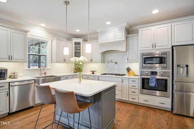 kitchen with stainless steel appliances, a sink, crown molding, light countertops, and hanging light fixtures