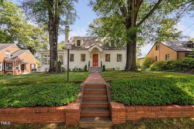 new england style home featuring a chimney and a front lawn